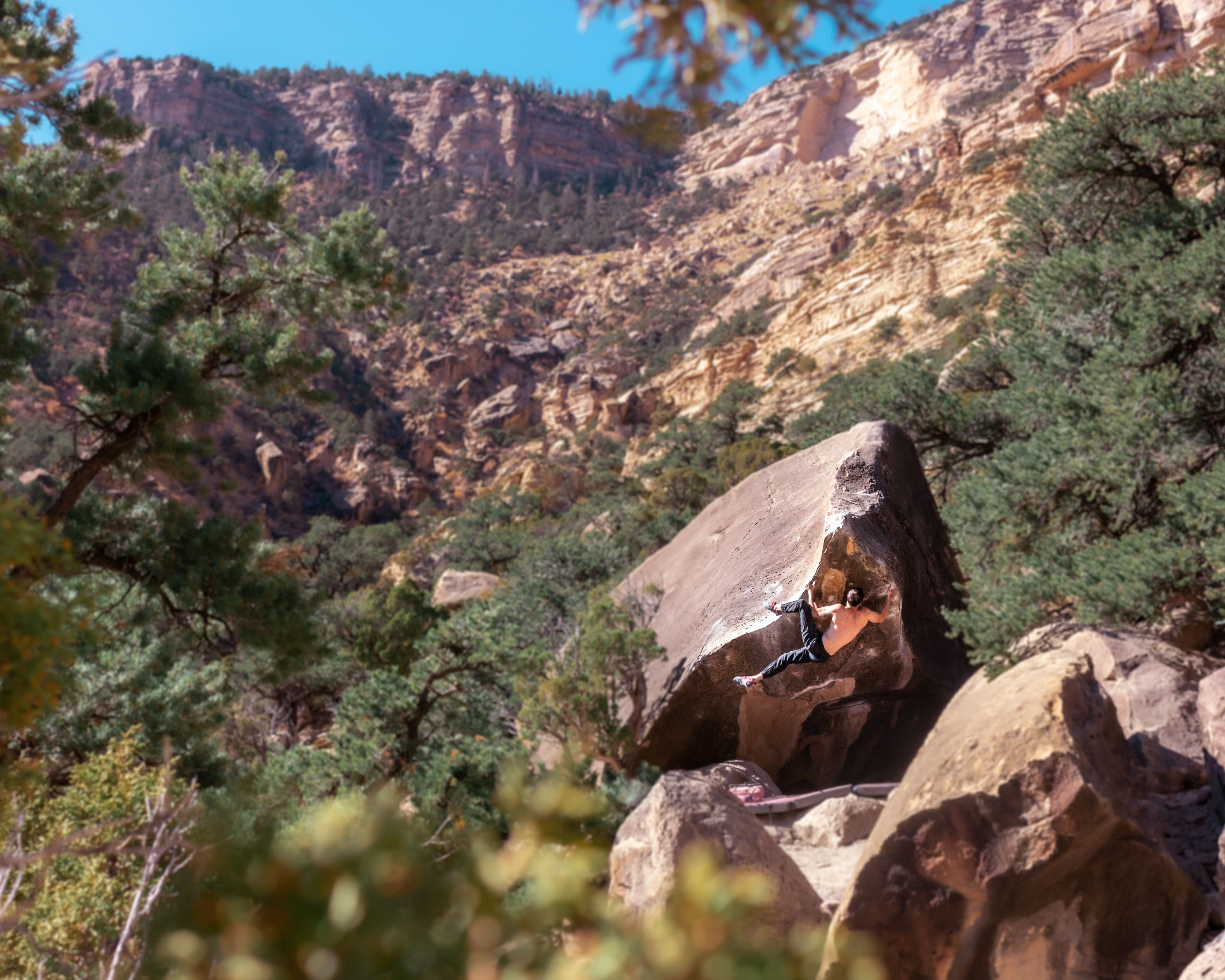 Scenic view of a mountainous landscape with rocks, trees, and a boulderer. Great White v6, Joe's Valley, Utah.