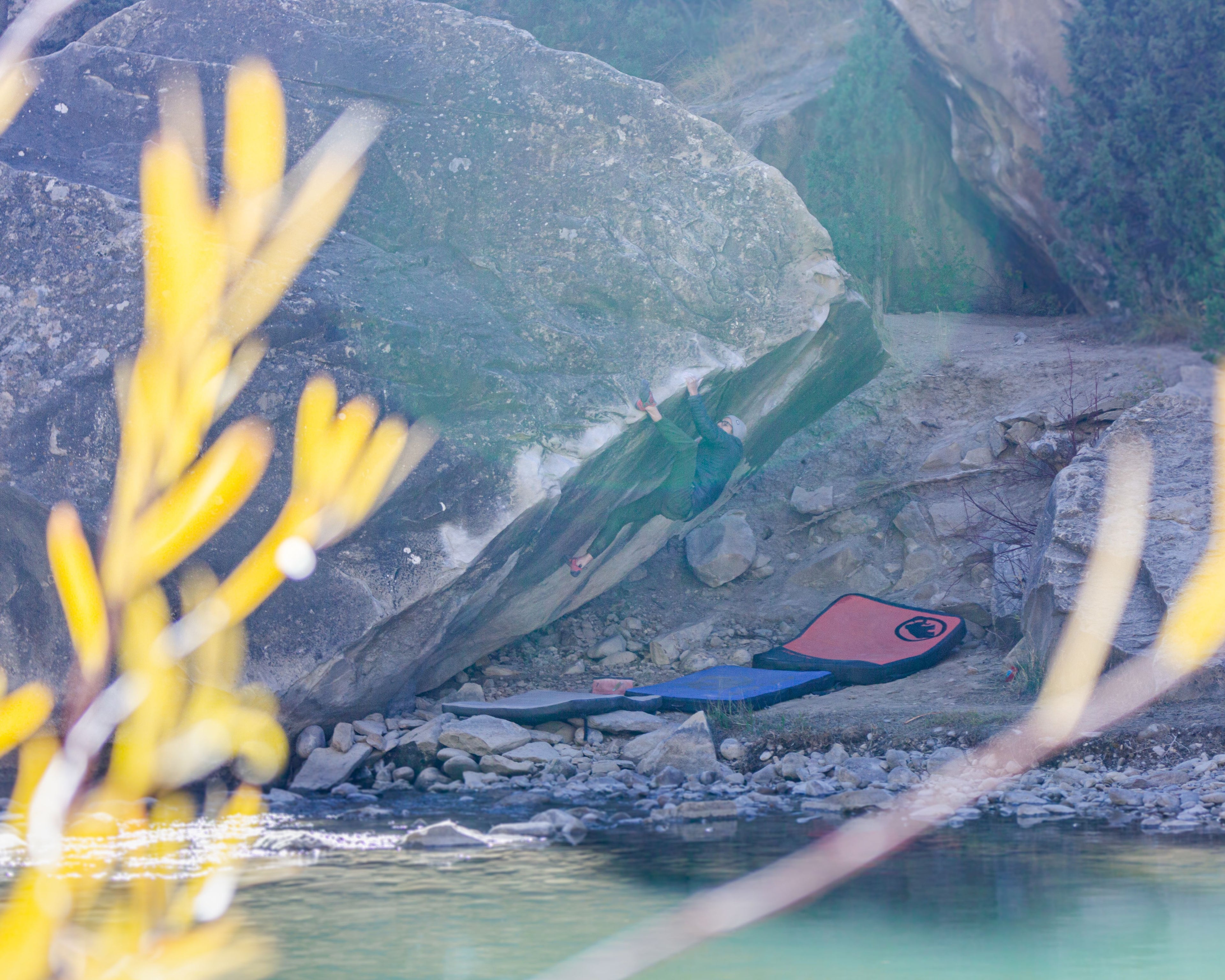 Boulderer on a traverse with water and plants in the foreground.