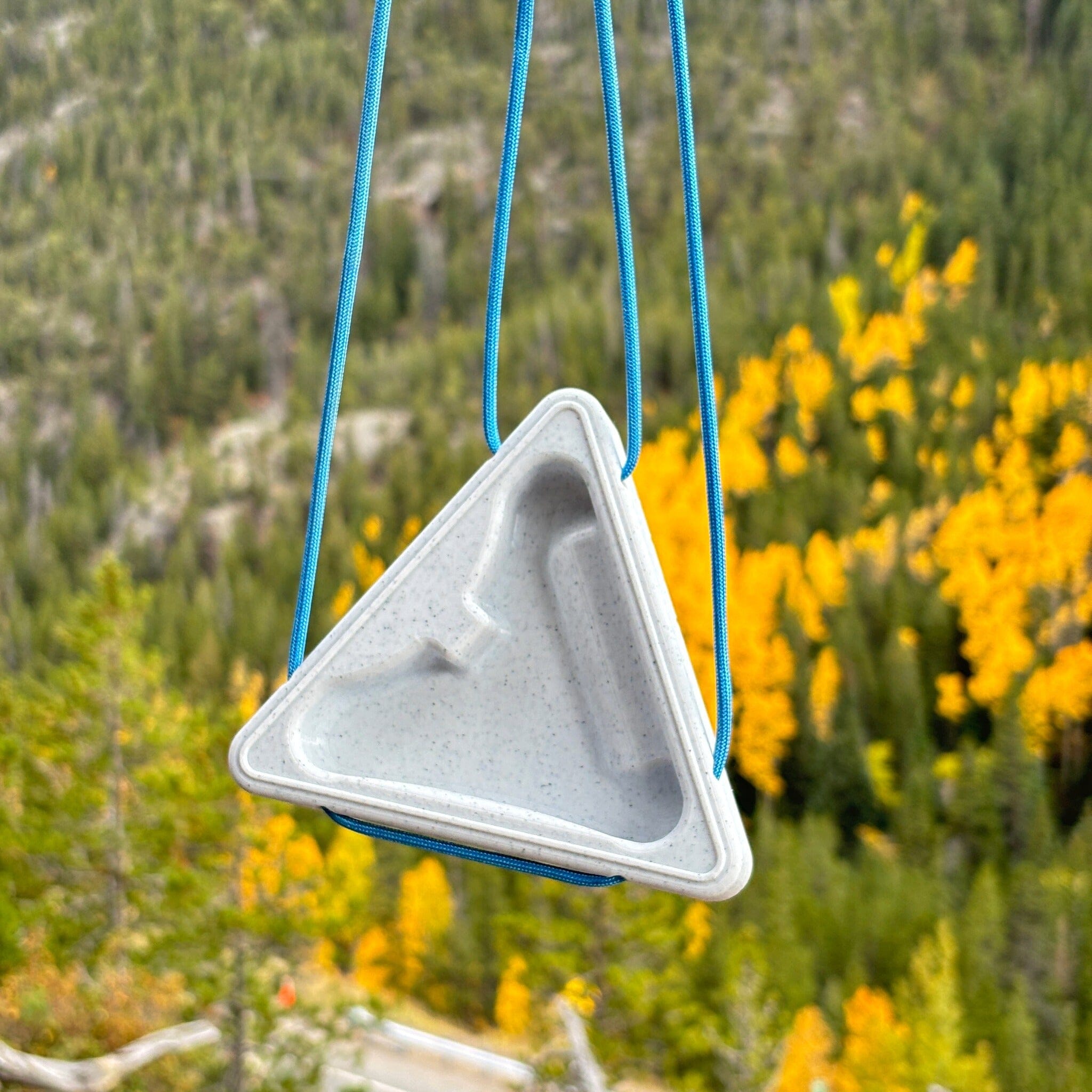Triangular warm up block hanging in front of a natural background of trees and fall foliage.