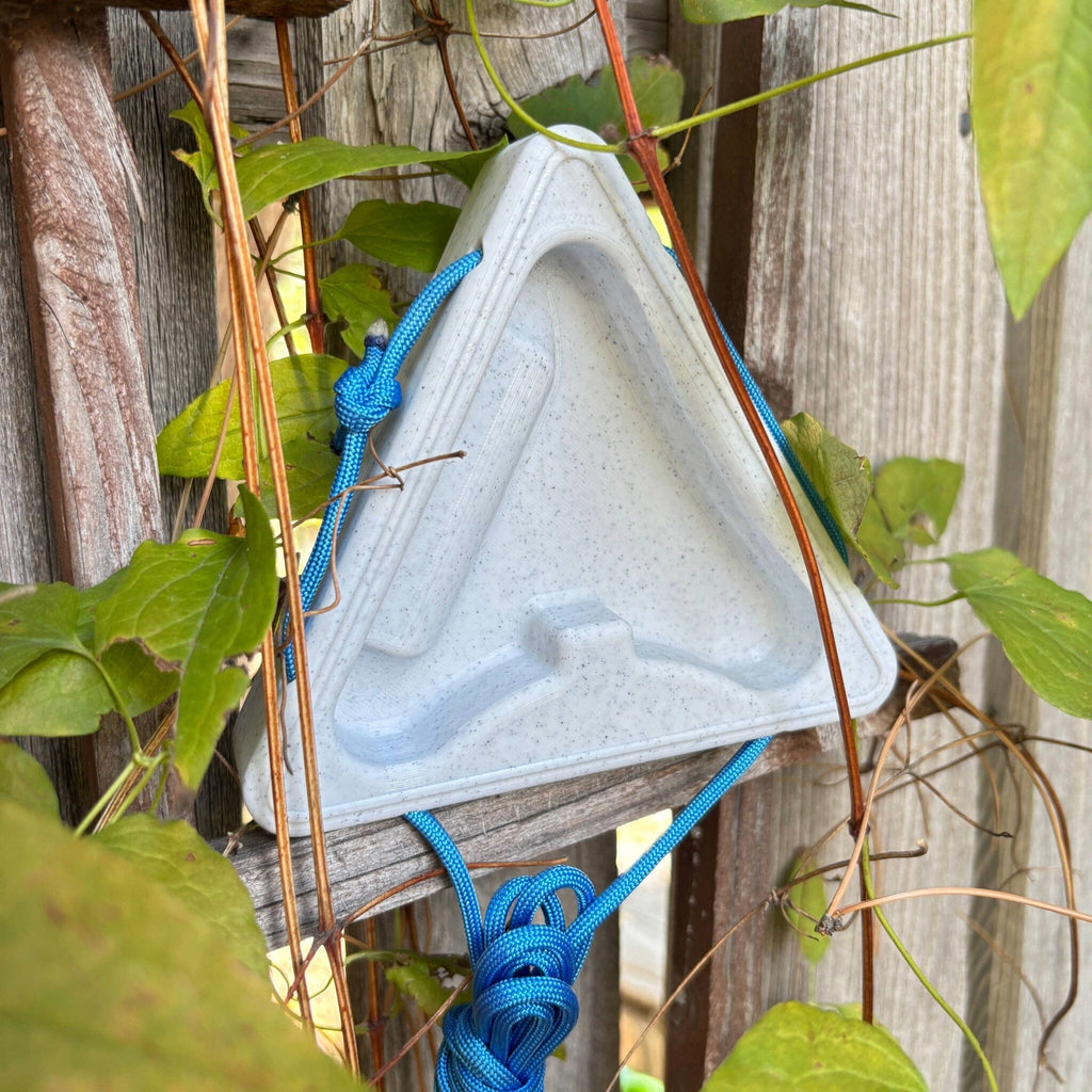 Triangular warm up block with blue cord attached, surrounded by vines on a fence.